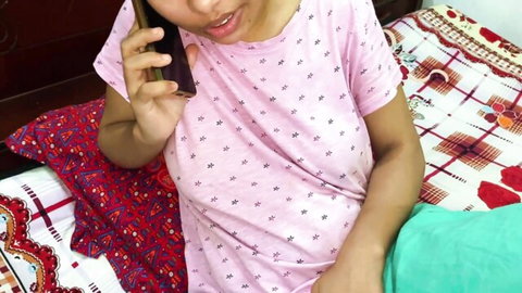 South Asian woman in pink polka-dot top talking on phone while sitting on colorful bed