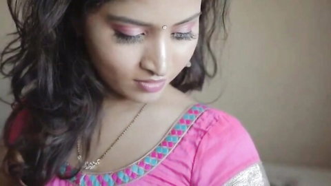 Sexy Indian babe in tight pink embroidered blouse smiling sensually with bindi and cleavage tease
