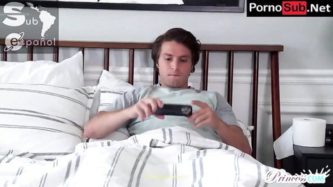 Young brown-haired guy lying in bed wearing t-shirt gripping phone intently