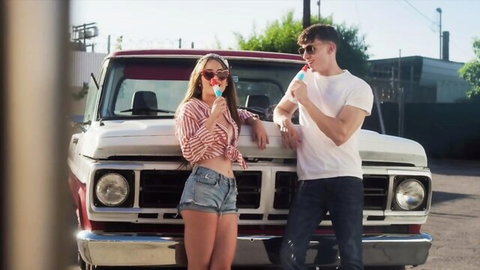 Lilly Bell in tied shirt and short shorts with stud by truck, teasing with popsicles