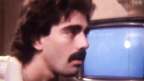 Retro 80s porn actor with curly hair and mustache in bedroom scene
