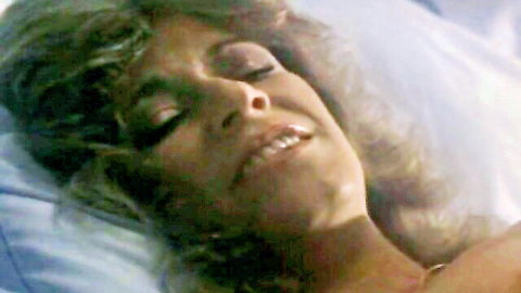 Blonde MILF with curly hair smiling seductively in bed