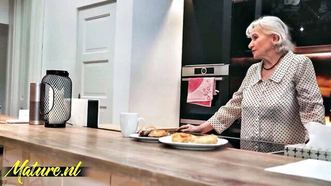Silver-haired granny in polka dot blouse stands at kitchen counter, Mature NL