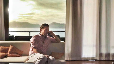 Vanessa Decker scene: handsome man in pink shirt on couch by sunset ocean view