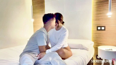 Passionate GILF kissing young stud on bed, intimate foreplay moment