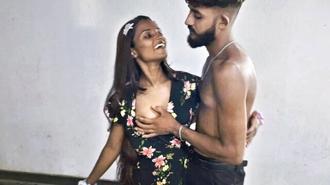 Smiling Indian cougar in floral dress embraced by shirtless muscular man