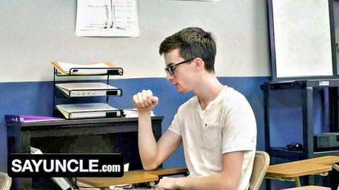 Glasses-wearing twink student sits pensively at classroom desk in gay taboo scene