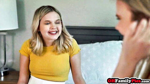 Two smiling blonde teen stepsisters teasing close-up on bed in yellow top and skirt