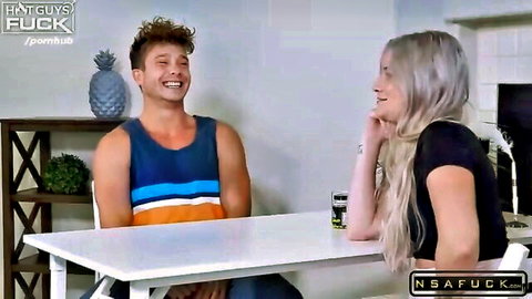 Smiling blonde babe in black top flirts with curly-haired stud in tank top at kitchen table before rough fuck