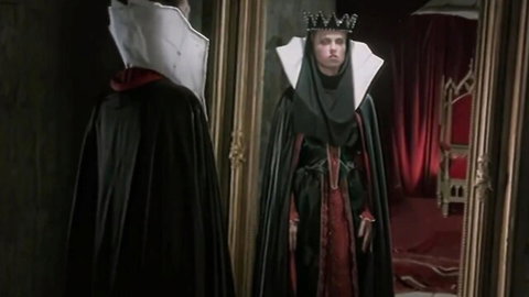 Evil Queen in Snow White cosplay stands before mirror in seductive gown