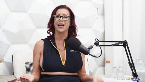 Busty redhead MILF with glasses teases massive cleavage in unzipped black top on mic