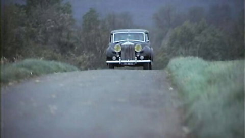 Vintage black luxury car driving on foggy rural road with greenery