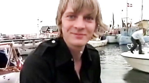 Retro blonde man in dark jacket by harbor boats, Expo Film XXX promo