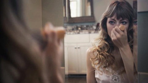 Young brunette in lacy lingerie holding orange puff to nose in bathroom mirror