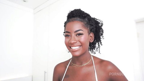 Smiling ebony beauty with curly hair and gold chain in tight white halter top showing cleavage