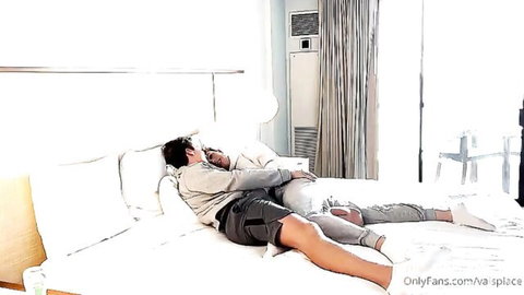 Two slim Asian guys cuddling spoon-style in bed, gay intimate moment