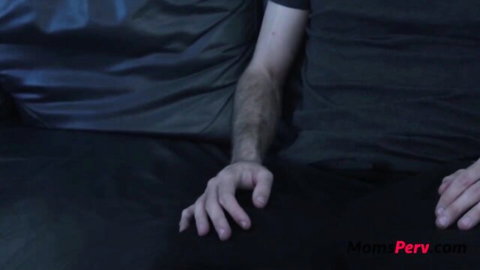 Hairy man's arm reaches for woman's hand on dark bed in steamy MomPerv taboo scene