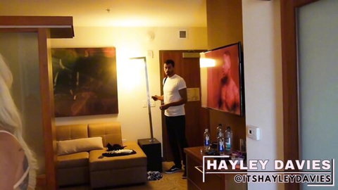 Tall black guy stands in hotel room with busty blonde art, Hayley Davies on TV, teasing promo vibe