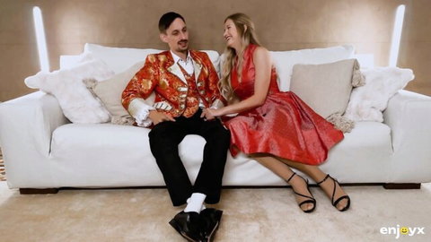 Blonde Stella Cardo in sexy red dress sitting with suited man on couch