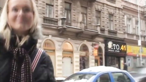 Smiling blonde woman in winter jacket on snowy Czech street near music club