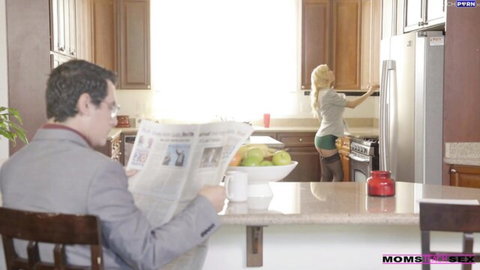 Blonde MILF in tiny denim shorts bends over showing ass cheeks while suited man reads newspaper in kitchen