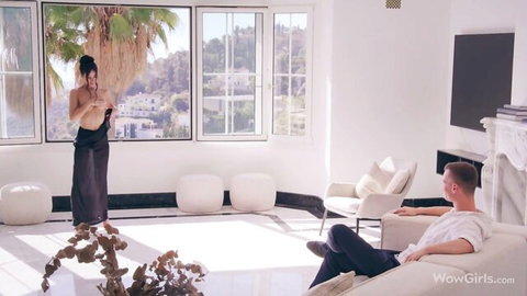 Kama Oxi topless in black skirt, boyfriend watching from couch