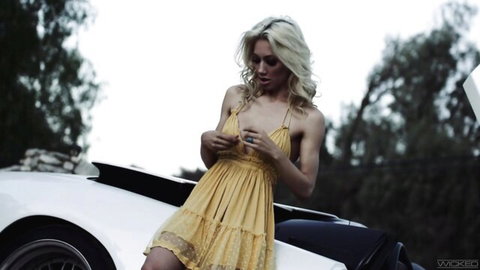 Blonde Ivy Wolfe in revealing yellow dress posing seductively on white sports car