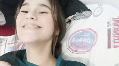 Smiling young woman with braces in teal top lying on bed, step-sis lingerie tease