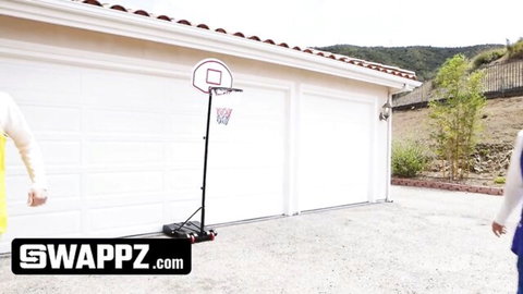 Swingers in sporty outfits stand by basketball hoop in driveway before wife swap