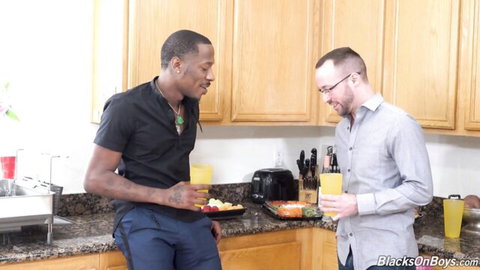 Tattooed black stud and glasses-wearing white guy flirt in kitchen holding drinks