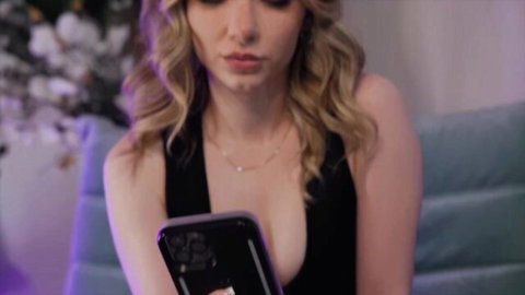 Young blonde teen with small tits showing deep cleavage in black top holding phone seductively