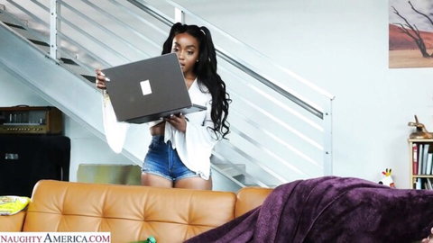 Curvy ebony babe with huge tits and big ass in tiny shorts holds laptop teasing cleavage.