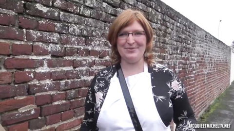 Smiling redhead MILF with glasses wearing black floral cardigan over white blouse against brick wall