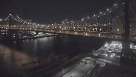 Aerial night view of illuminated Brooklyn Bridge spanning dark river with docked ships
