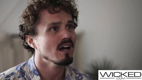 Curly-haired man with mustache in floral Hawaiian shirt looking sideways