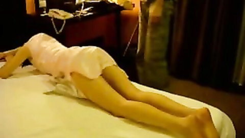 Brunette wife lying prone on hotel bed with pink dress hiked up exposing bare ass and long legs