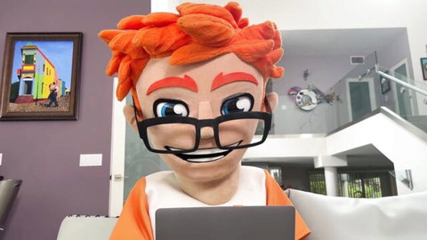 Orange furry mascot with glasses smiling while using laptop on couch in modern living room