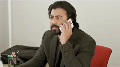 Bearded man in suit jacket talks on phone at desk, office setting