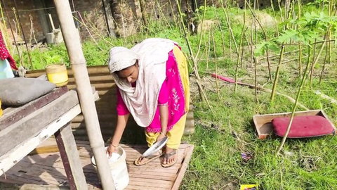Indian village woman in pink salwar kameez bending over outdoors