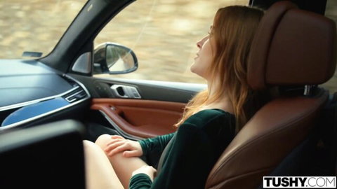 Redhead in green dress moans with eyes closed spreading legs in luxury car