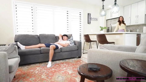 Busty MILF stepmom in yellow top watches stepson lounging on couch in living room