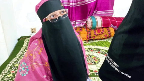 Niqabi woman with pink glasses sitting on colorful cushions in bedroom