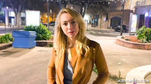 Blonde woman in tan leather jacket poses seductively on nighttime urban street