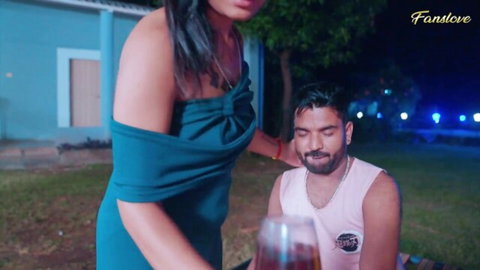 Sexy South Asian woman in tight teal off-shoulder dress teases bearded hunk with drink outdoors