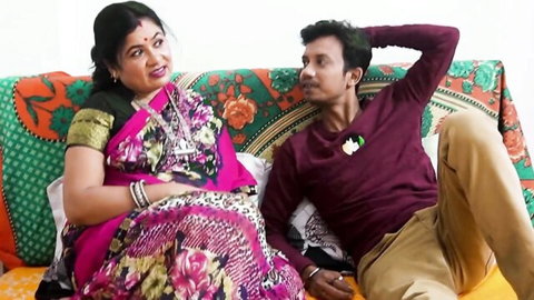 Smiling curvy Indian woman in pink saree sits intimately with handsome man on colorful couch