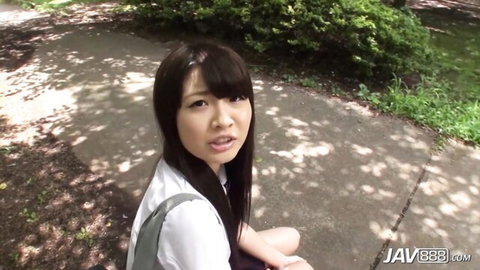 Skinny Japanese schoolgirl in white uniform blouse and skirt sitting outdoors on path with teasing expression