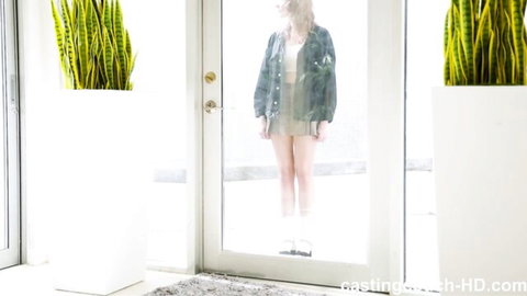 Blonde babe in denim shorts and jacket standing behind glass door, teasing pose