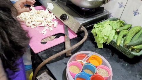 South Asian woman chopping white veggies on pink board in cluttered Indian kitchen