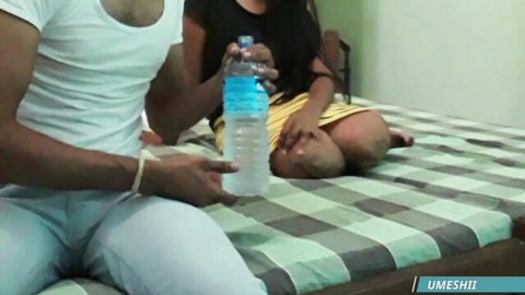 Muscular Sri Lankan guy in tight white shorts holds water bottle to young South Asian babe in yellow skirt on bed
