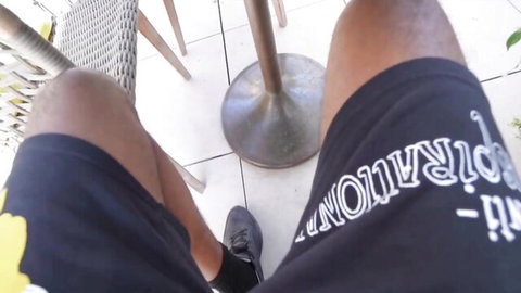 POV closeup of muscular ebony man's thick thighs in black shorts on tiled outdoor patio